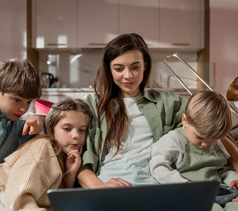 An adult and three children sit together looking at a laptop on a couch.