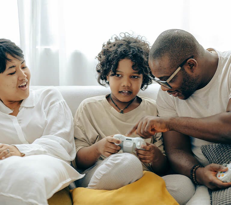 Two parents and a child sit on a couch enjoying playing video games together.