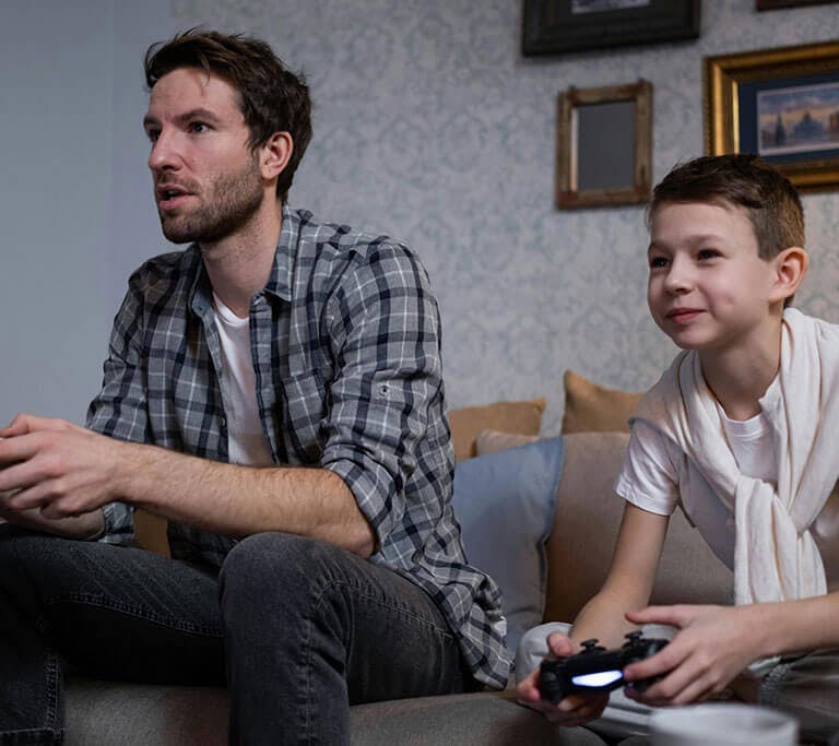 Two people sitting on a couch playing a video game together, each holding a game controller, focused and smiling in a cozy living room setting.