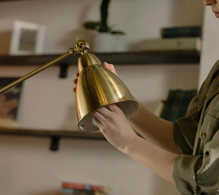A person changing an LED light bulb on a brass lamp.